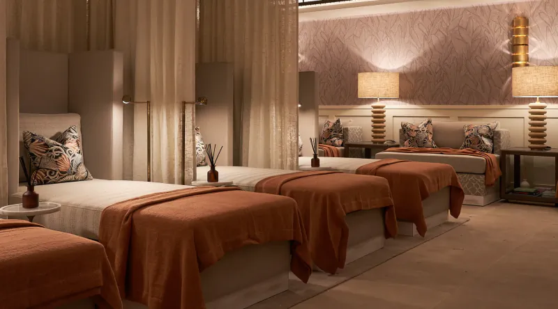 Luxury hotel room with three single beds, burnt orange throws, patterned pillows, and warm lighting