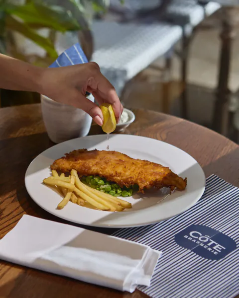 Hand squeezing lemon over fish and chips at Côte Brasserie