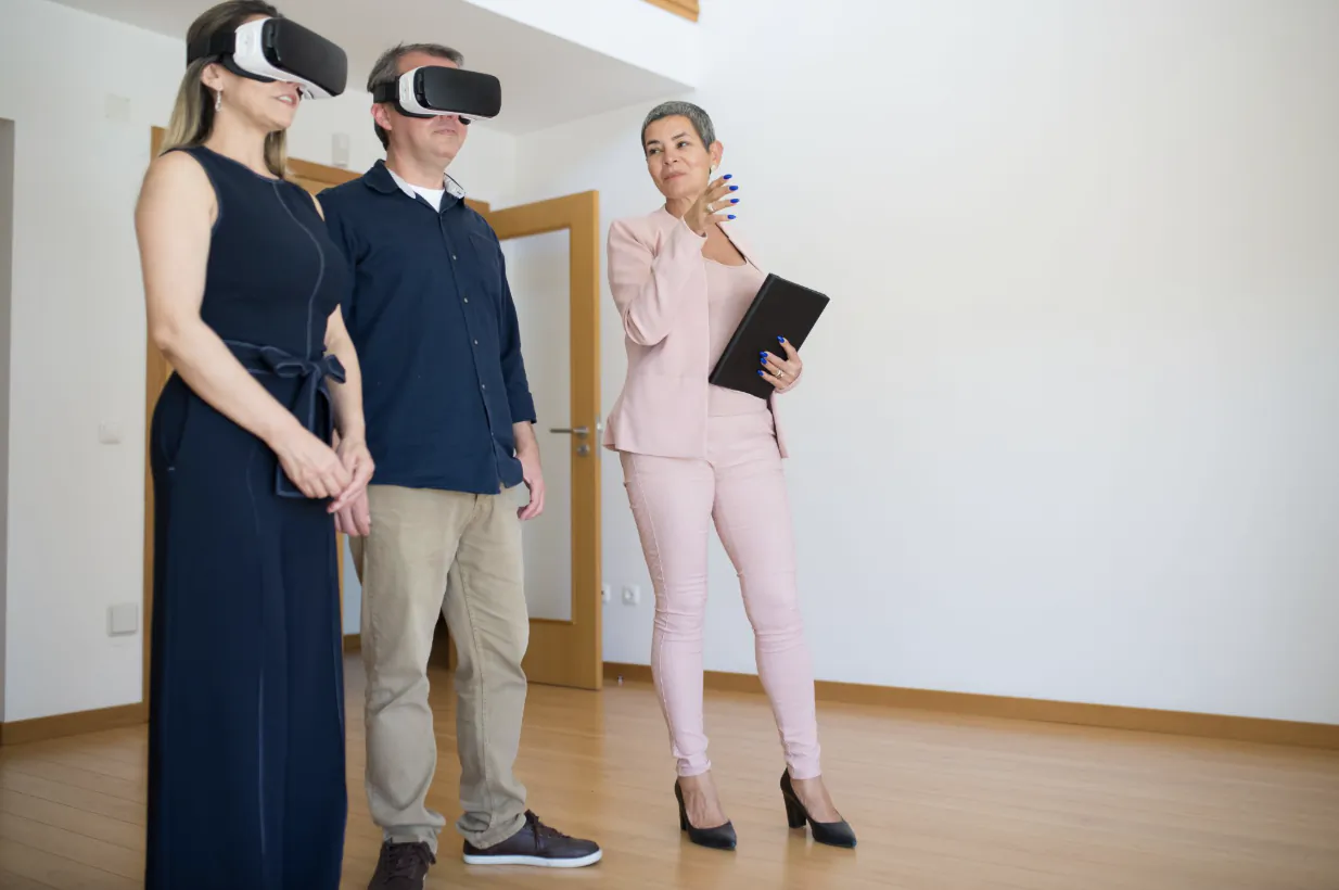 Three professionals in an empty room wearing VR headsets, one woman holding a tablet and gesturing thoughtfully
