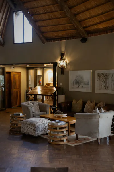 Luxury safari lodge lounge with high wooden ceiling, grey armchairs, patterned ottoman, and wall art
