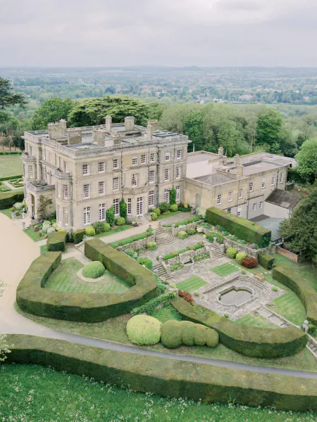 Aerial view of Hedsor House, a grand stone mansion with formal gardens, manicured hedges, and a fountain overlooking the English countryside
