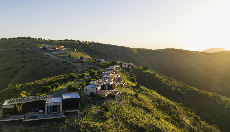 Aerial view of modern hillside villas at sunset on a lush green slope, with golden light illuminating the landscape