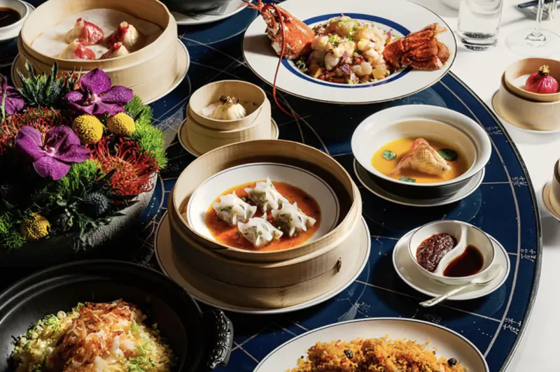 Elegant Chinese dim sum banquet on a blue lazy Susan with dumplings, lobster, fried rice, and floral centerpiece