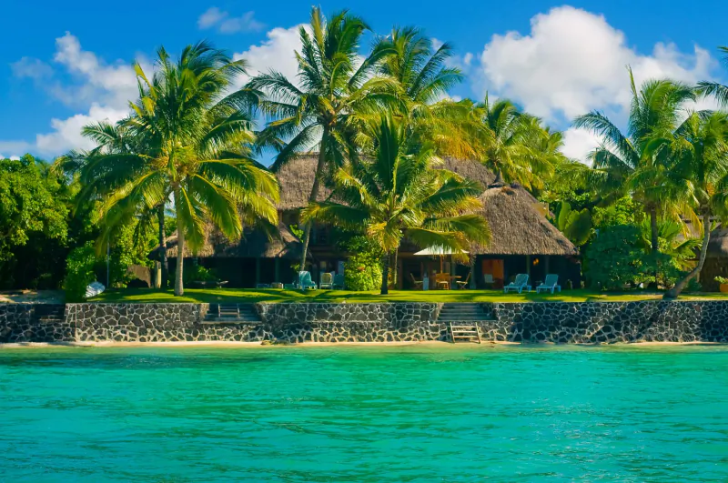Overwater bungalows with thatched roofs on a tropical island, surrounded by palm trees and turquoise water