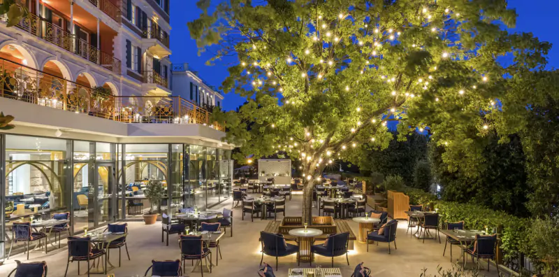 Hotel Imperial Dubrovnik outdoor terrace with tables, chairs and a large tree strung with lights at dusk