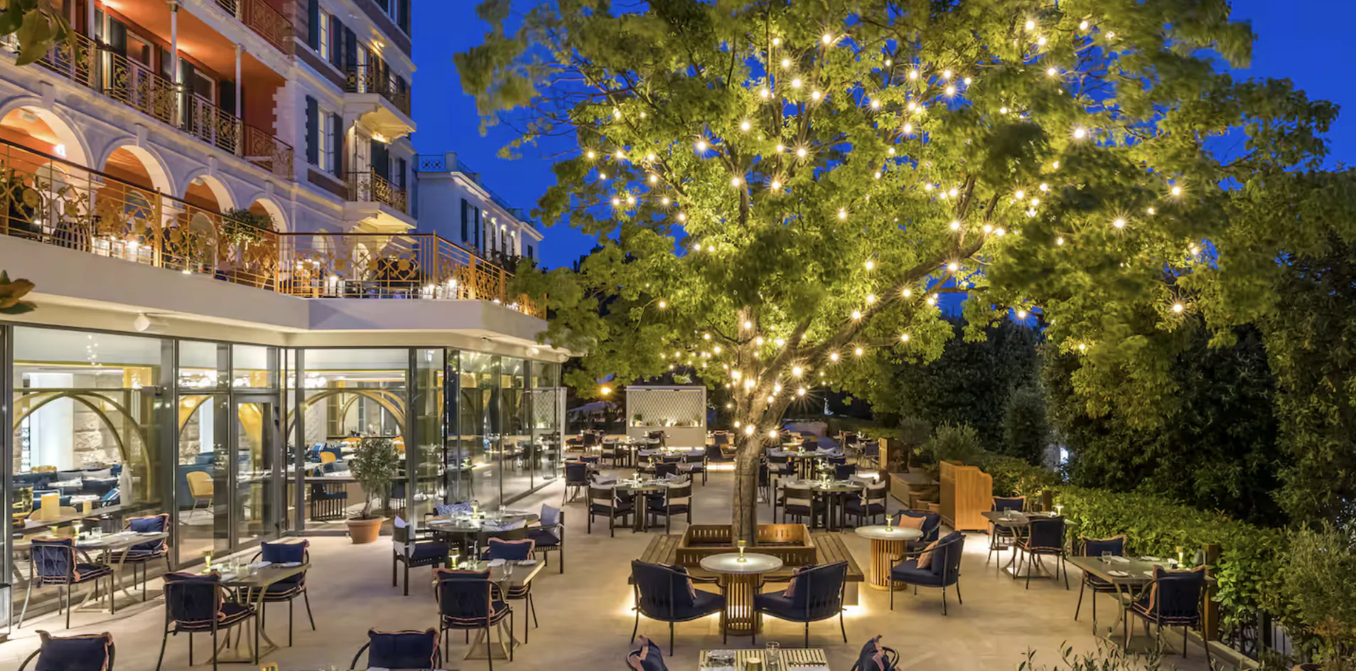 Hotel Imperial Dubrovnik outdoor terrace with tables, chairs and a large tree strung with lights at dusk