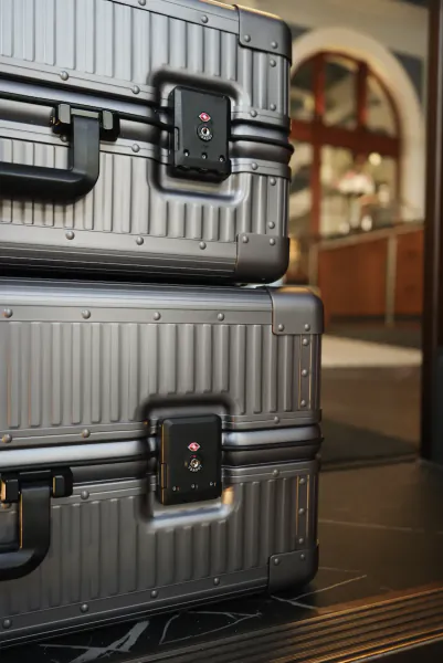 Two stacked silver aluminum suitcases with black handles and TSA locks, displayed in a luxury store