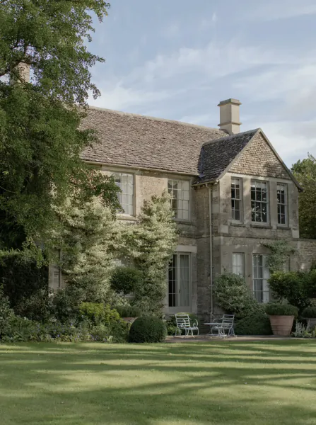 Stone country house with lawn, garden furniture, and trees under a blue sky