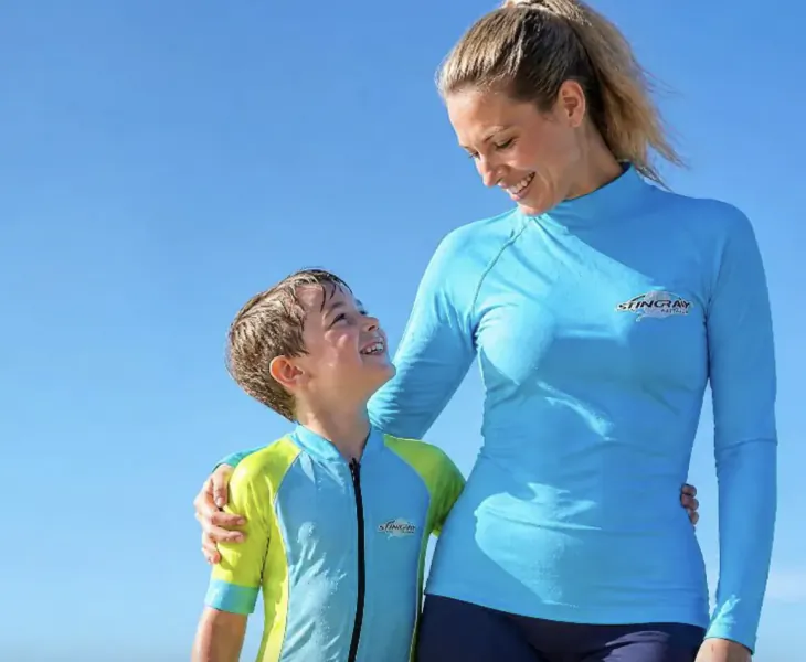 Woman and boy in matching blue and yellow sun protection shirts smiling outdoors under clear blue sky