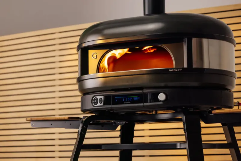 Gozney pizza oven with visible flames inside, digital display showing 842°F on a stand
