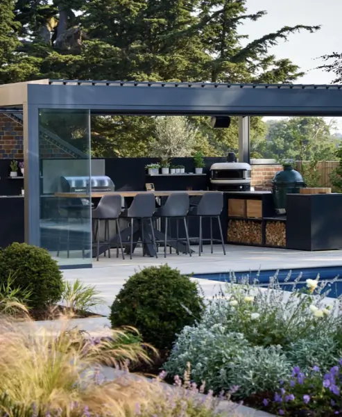 Modern outdoor kitchen with bar stools under a glass and metal pergola beside a swimming pool