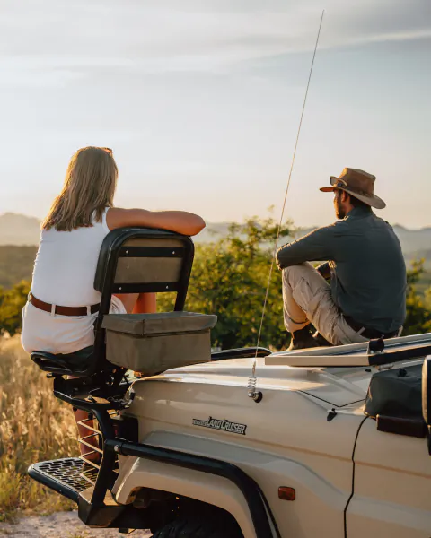 Couple seated on a safari vehicle overlooking a scenic landscape at sunset
