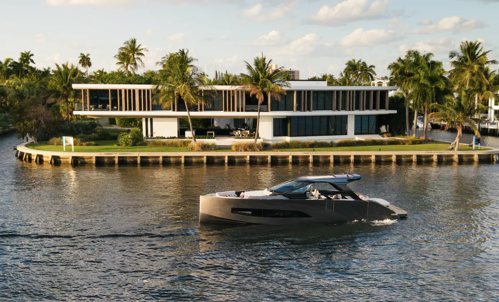 Modern gray yacht cruising past a waterfront luxury home with palm trees