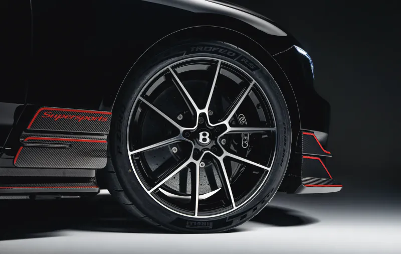 Close-up of black Bentley Supersports wheel with carbon fiber side skirt and red accents