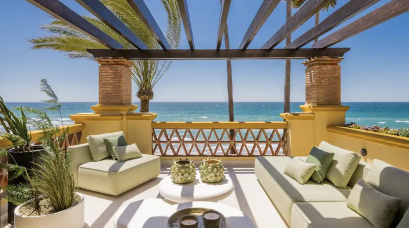 Luxury oceanfront patio with beige sofas, round coffee table, and sea view under wooden pergola