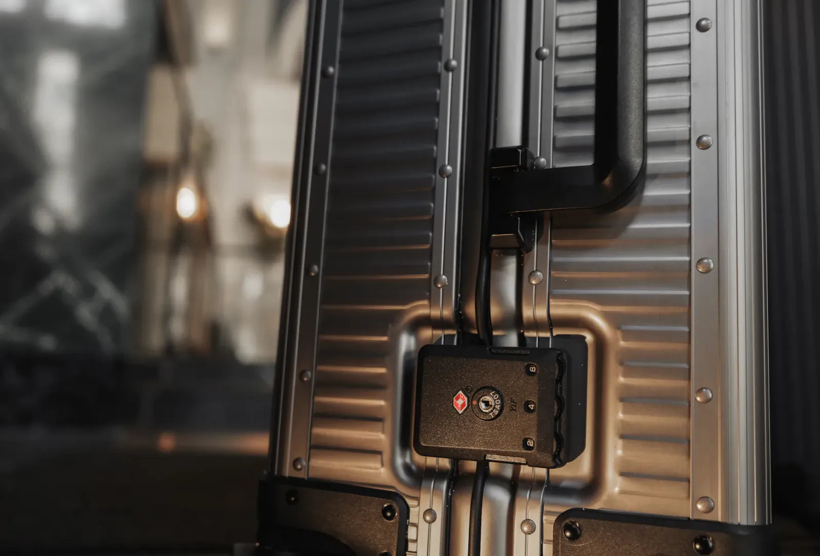 Close-up of a silver hard-shell suitcase with black handle and TSA lock featuring the Louré logo