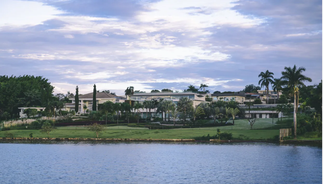 Lakeside view of large waterfront homes with palm trees and manicured lawns under a cloudy sky