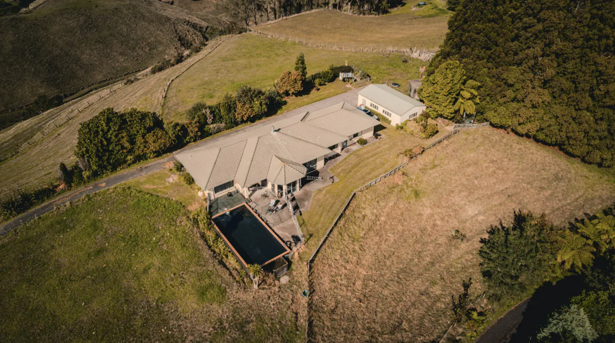 Aerial view of a large modern farmhouse with pool and surrounding rural fields in New Zealand