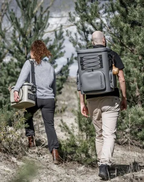 Man and woman walking away on a forest trail, carrying large grey coolers on their backs