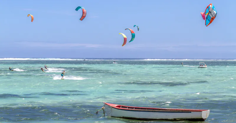 Kite surfers on turquoise ocean with colorful kites flying above, small boat in foreground