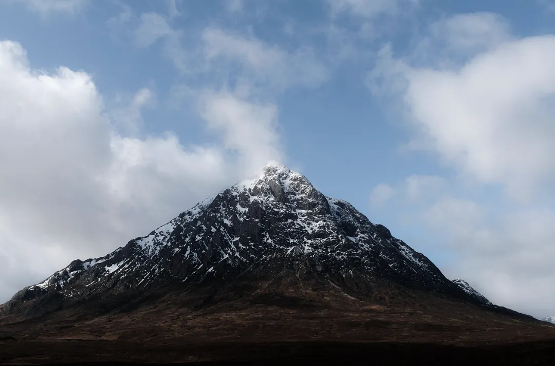 Snow-capped mountain peak under a blue sky with white clouds