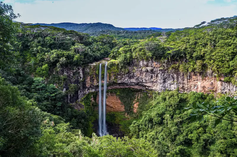 Twin waterfalls cascading down a lush green cliff into a dense tropical forest in Mauritius