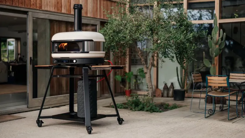 Gozney pizza oven on black stand with visible fire, outdoor patio setting
