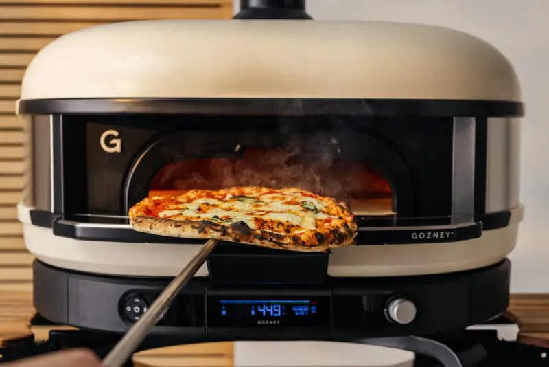 Gozney pizza oven with a cooked pizza on a peel being pulled from the glowing interior