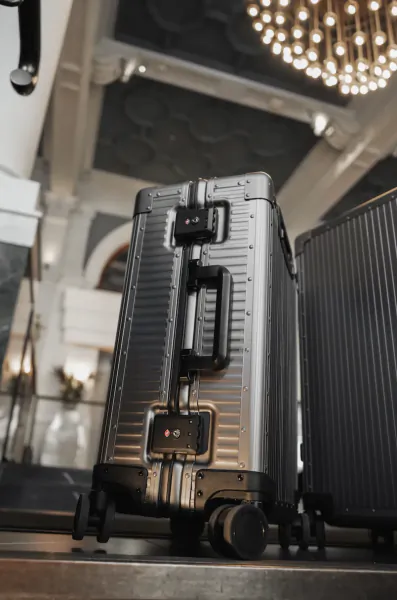 Two silver hard-shell suitcases with black accents stand on a polished floor in a grand hotel lobby with a crystal chandelier overhead