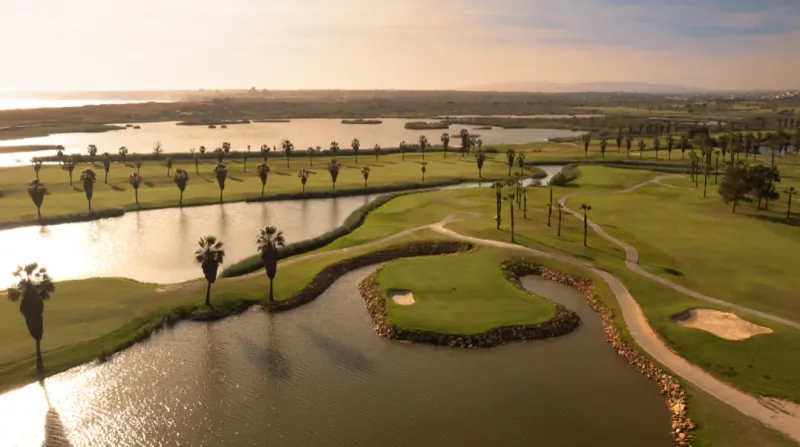Aerial view of a lush golf course with winding fairways, sand traps, palm trees, and water hazards at sunset