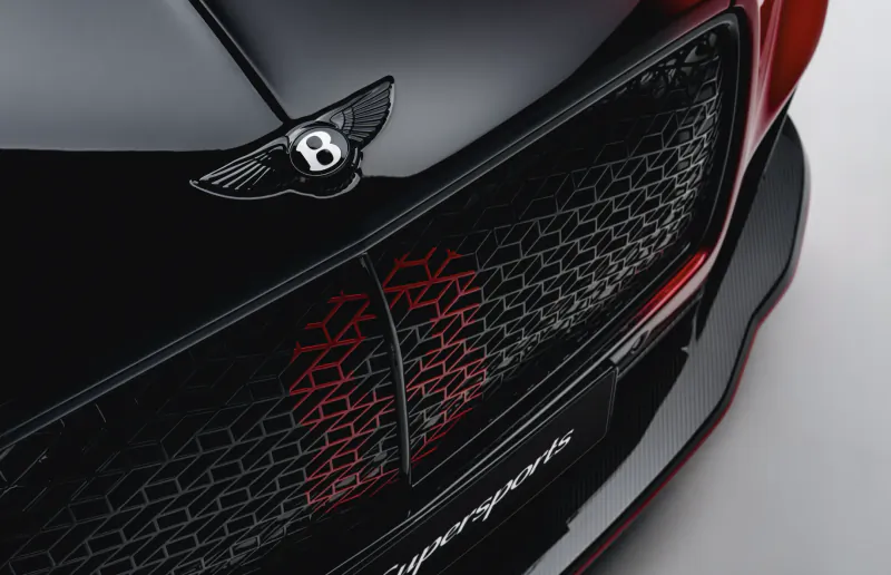 Close-up of Bentley Supersports front grille with red accents, Flying B emblem, and carbon fiber trim