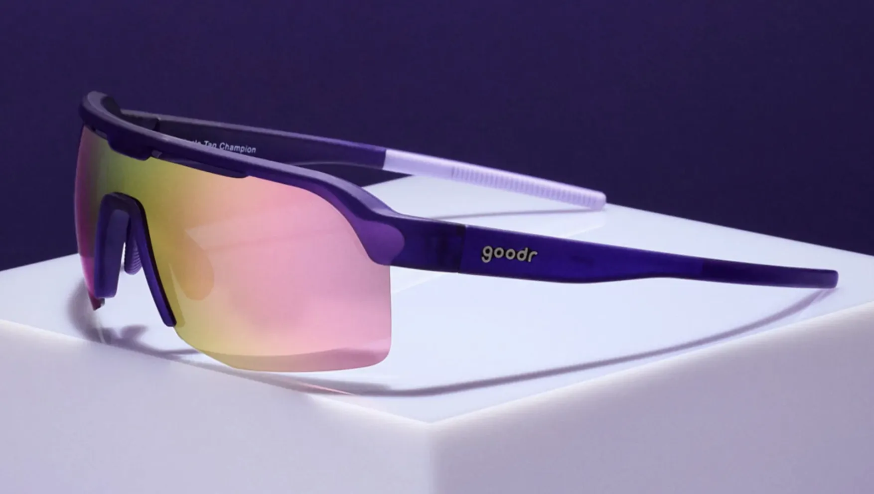 Purple and white goodr sunglasses with pink-to-yellow gradient lenses on a white display stand