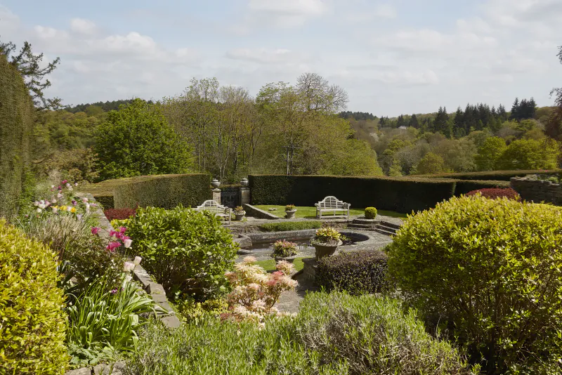 Formal garden with circular pond, white bench, and lush flower beds at Hedsor House