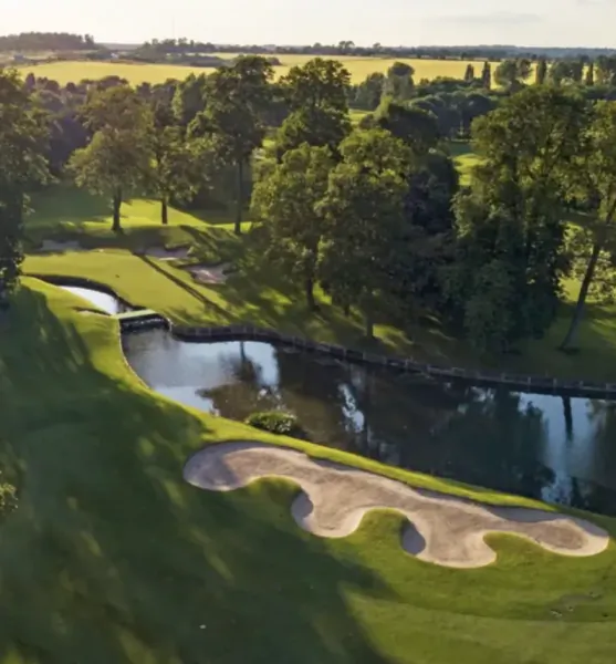 Aerial view of a golf course with a winding water hazard, sand bunkers, and lush green fairways surrounded by trees