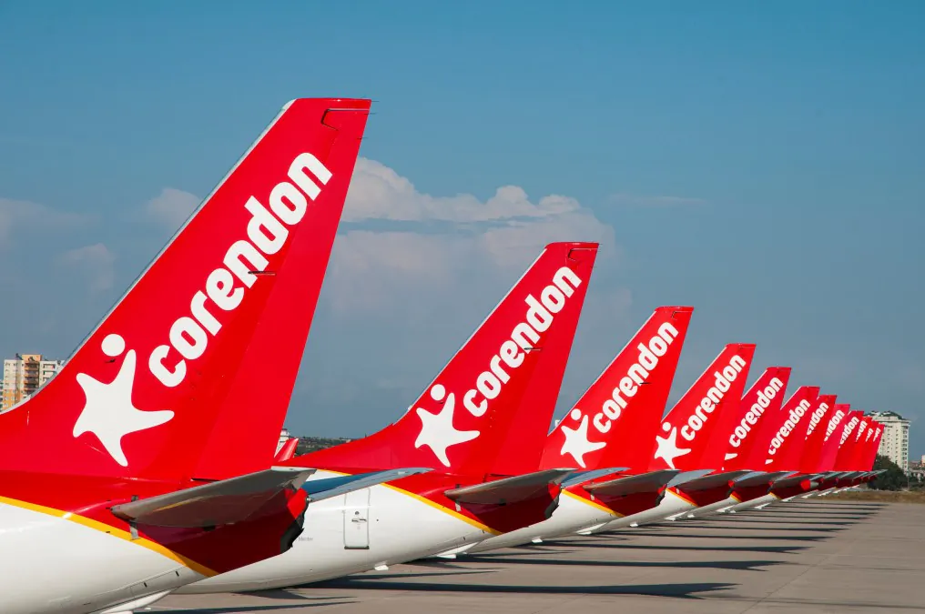 Row of Corendon Airlines red airplane tails lined up on the tarmac under a clear blue sky