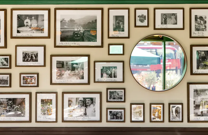 Wall of framed black-and-white photos with a round window showing a red double-decker bus outside