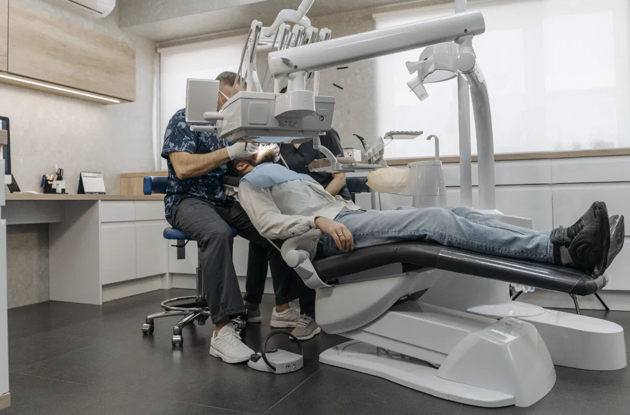 Dentist in blue shirt operating overhead equipment on reclined patient in modern dental clinic