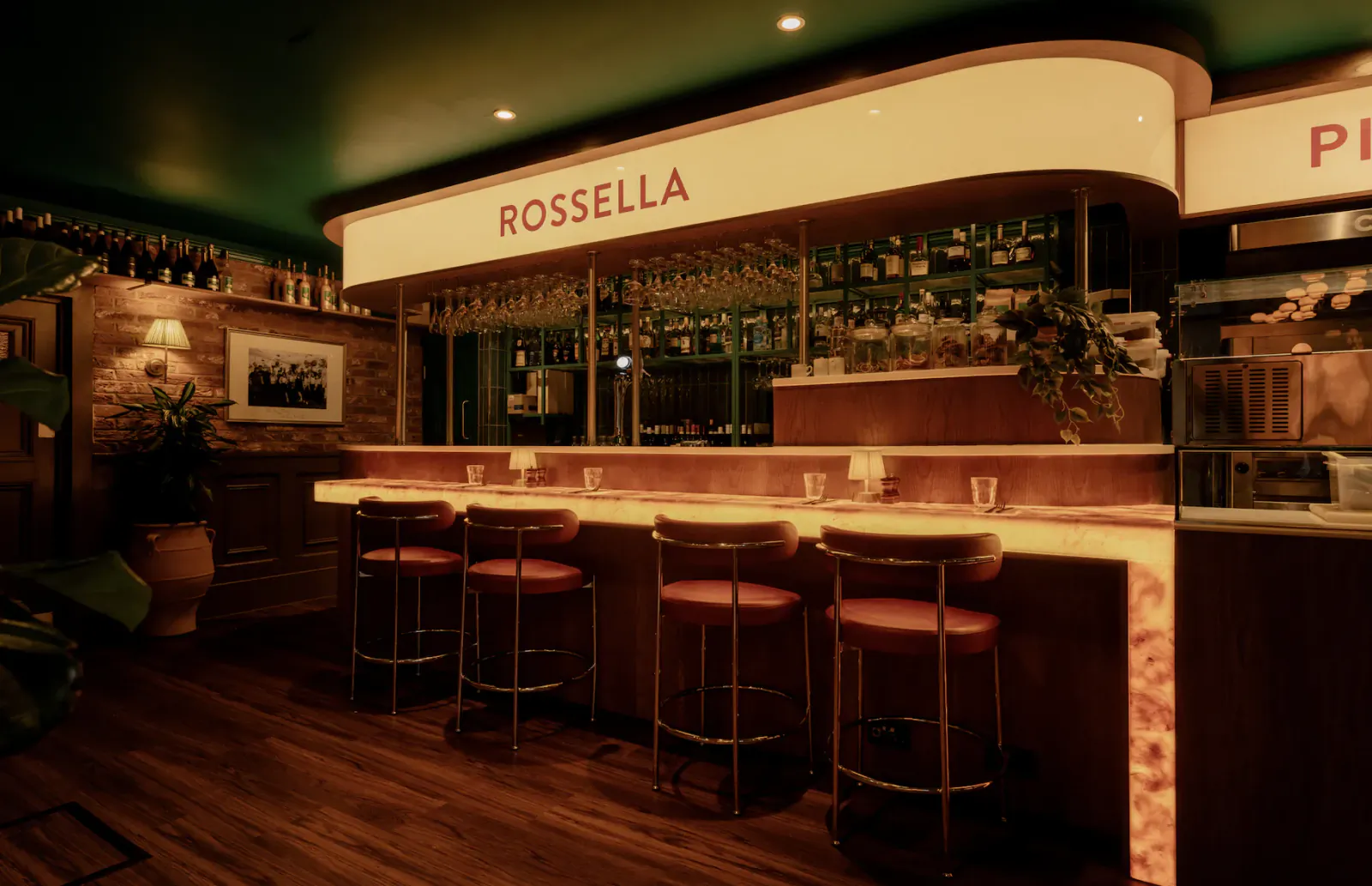 Rossella bar with red stools, marble counter, hanging glasses and backlit bottles