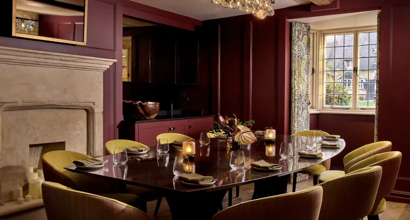Elegant dining room with dark red walls, marble fireplace, and large wooden table set with candles and yellow chairs