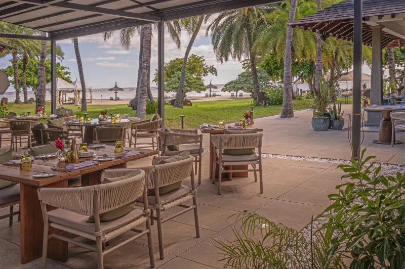 Elegant outdoor restaurant at Maradiva Villas Resort & Spa with wooden tables, woven chairs, and ocean view through palm trees