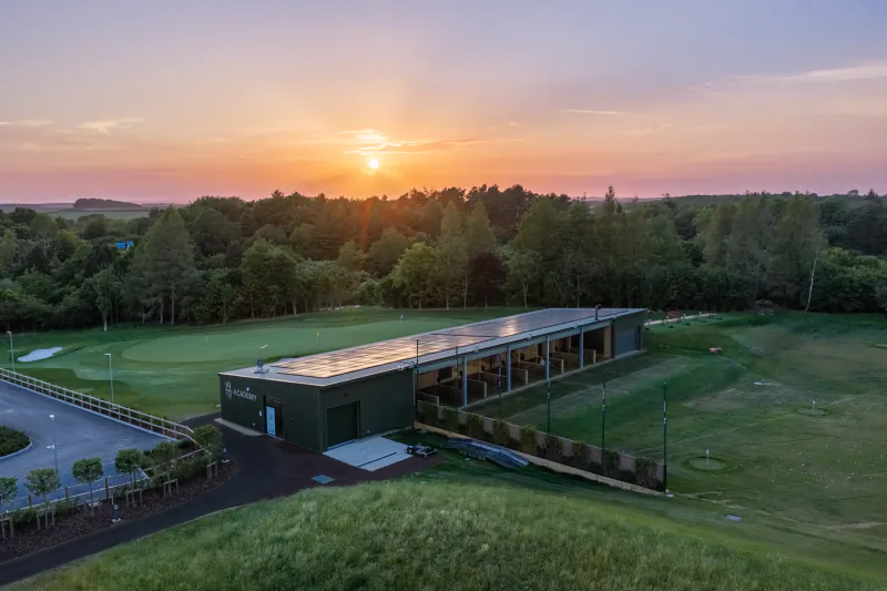 Aerial sunset view of Basingstoke Golf Club's modern clubhouse with solar panels overlooking the green course and trees