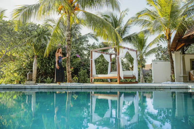 Woman in black dress standing by palm tree near poolside canopy bed at Maradiva Villas Resort & Spa