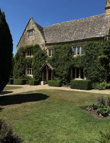 Stone house with ivy-covered walls, gabled roof, and manicured garden under blue sky