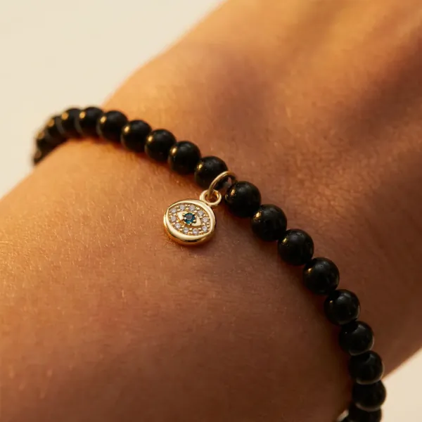 Close-up of a wrist wearing a black beaded bracelet with a small gold evil eye charm set with blue stones