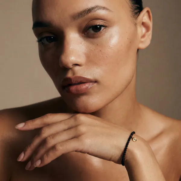 Close-up of a woman with glowing skin wearing a black beaded bracelet with gold crescent moon charm on her wrist