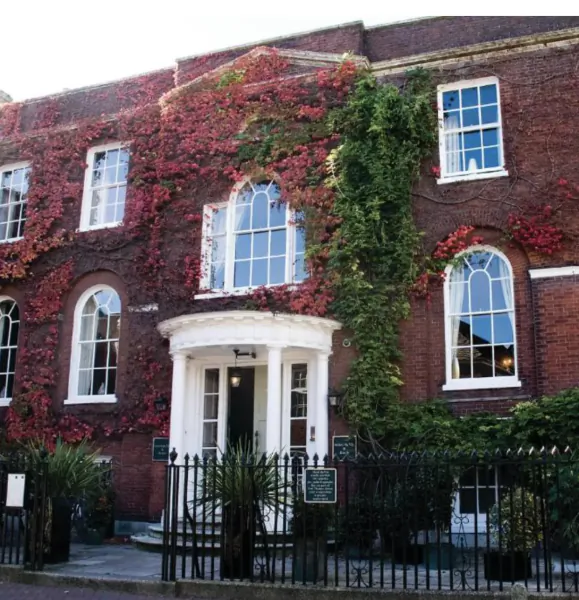 Brick townhouse covered in red and green ivy with white arched doorway and windows