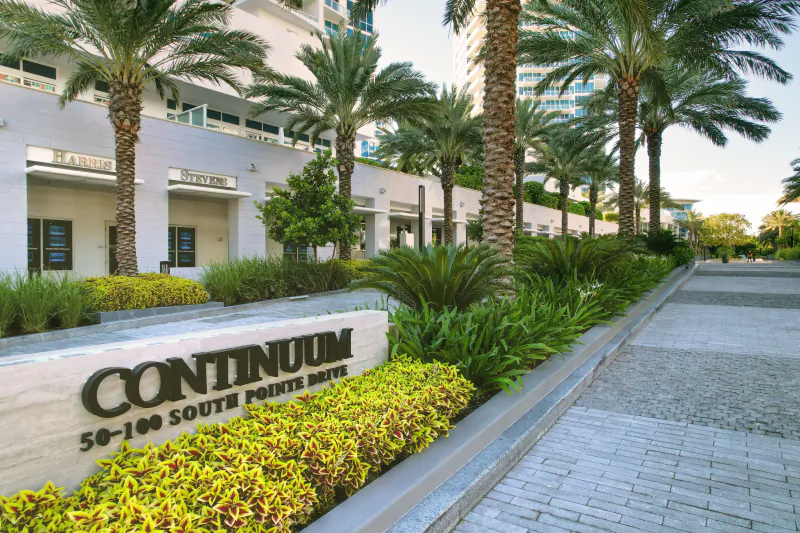 Continuum luxury condo entrance with large stone sign, palm trees, and modern white building in Miami Beach