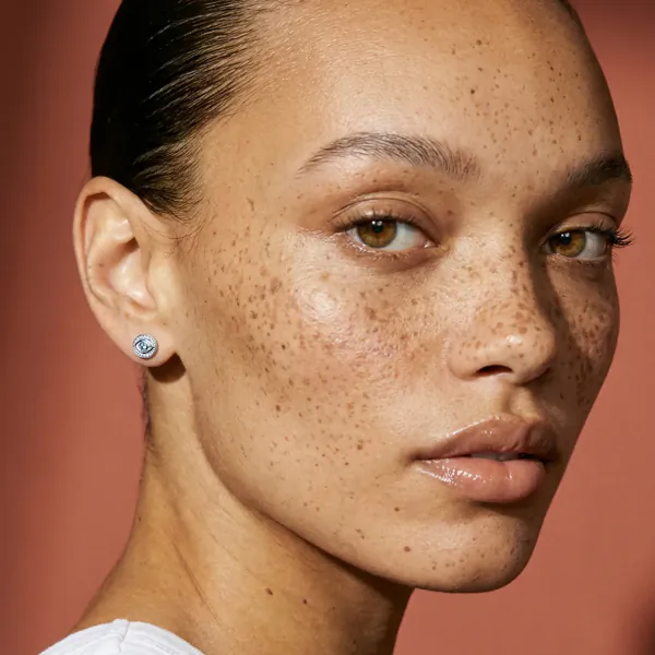 Close-up of a woman with freckled skin wearing a small circular silver earring with blue and white design