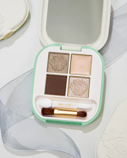 Open Paul & Joe eyeshadow palette with four floral-embossed shades, mirror, and dual-ended brush on white surface