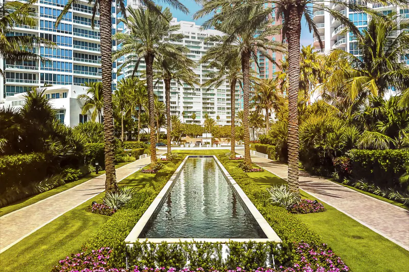 Long rectangular reflecting pool lined with tall palm trees and lush gardens, Continuum luxury high-rises in the background